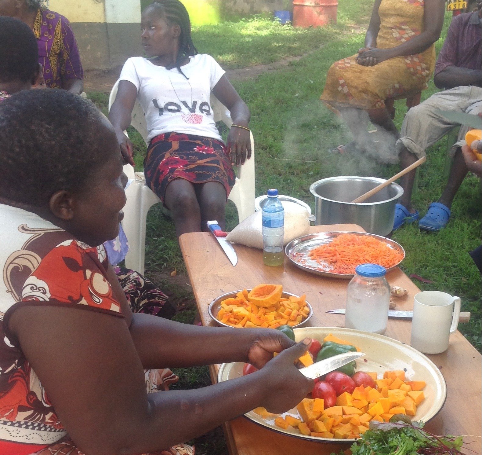A group of people sitting around a table while one prepares fresh vegetables